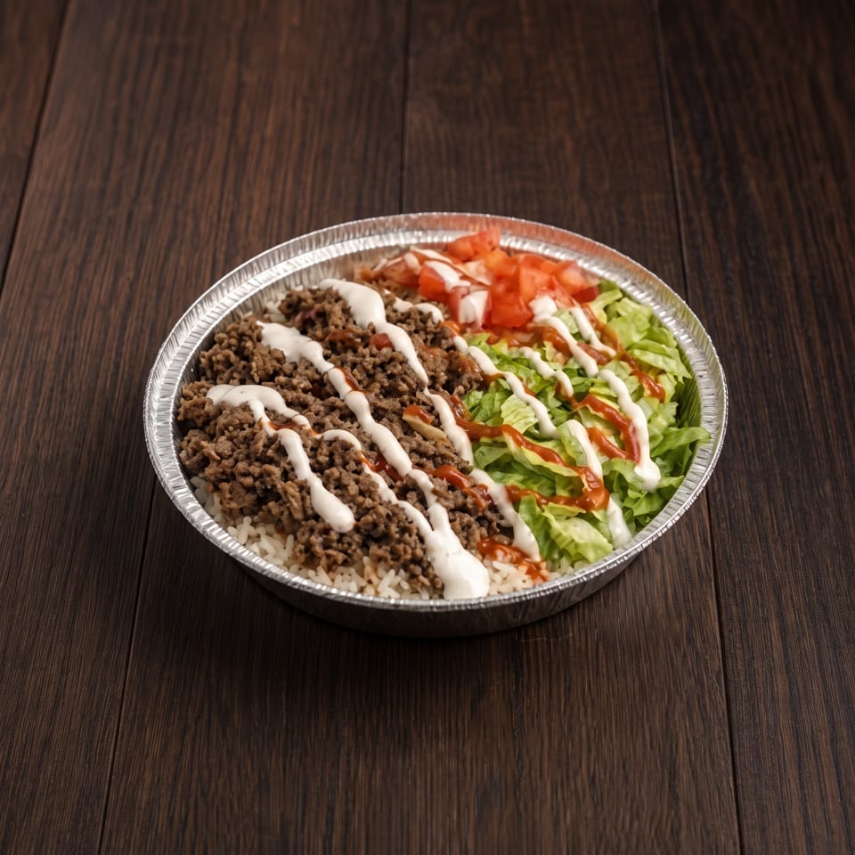 Ground beef and rice bowl topped with lettuce, tomatoes, and drizzled white and red sauces in a foil tray.